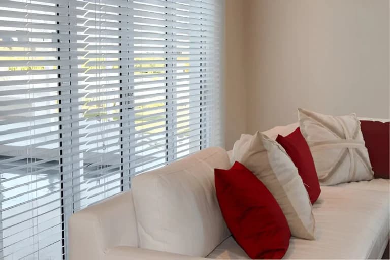 White plantation shutters beside a sofa with red and white cushions